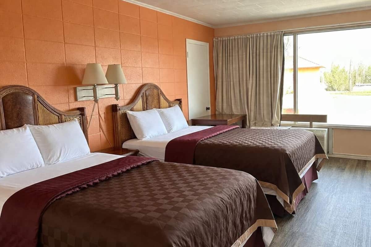 A hotel room with two beds, a window with curtains, a lamp, and a ceiling light.