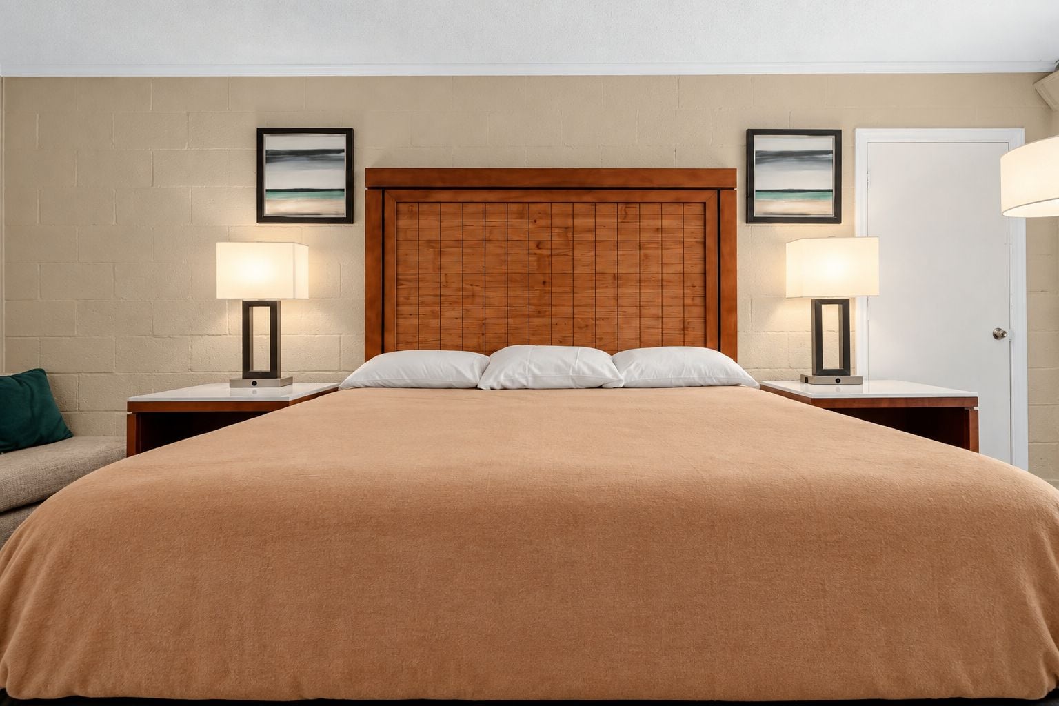 Une chambre d’hôtel avec un grand lit, deux lampes de chevet, une tête de lit en bois et une porte.