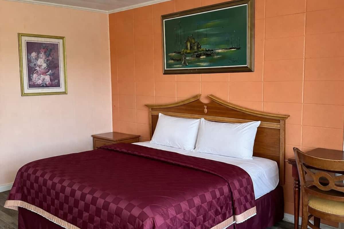 A hotel room with a large bed, a wooden headboard, a painting on the wall, and a small table with a chair.