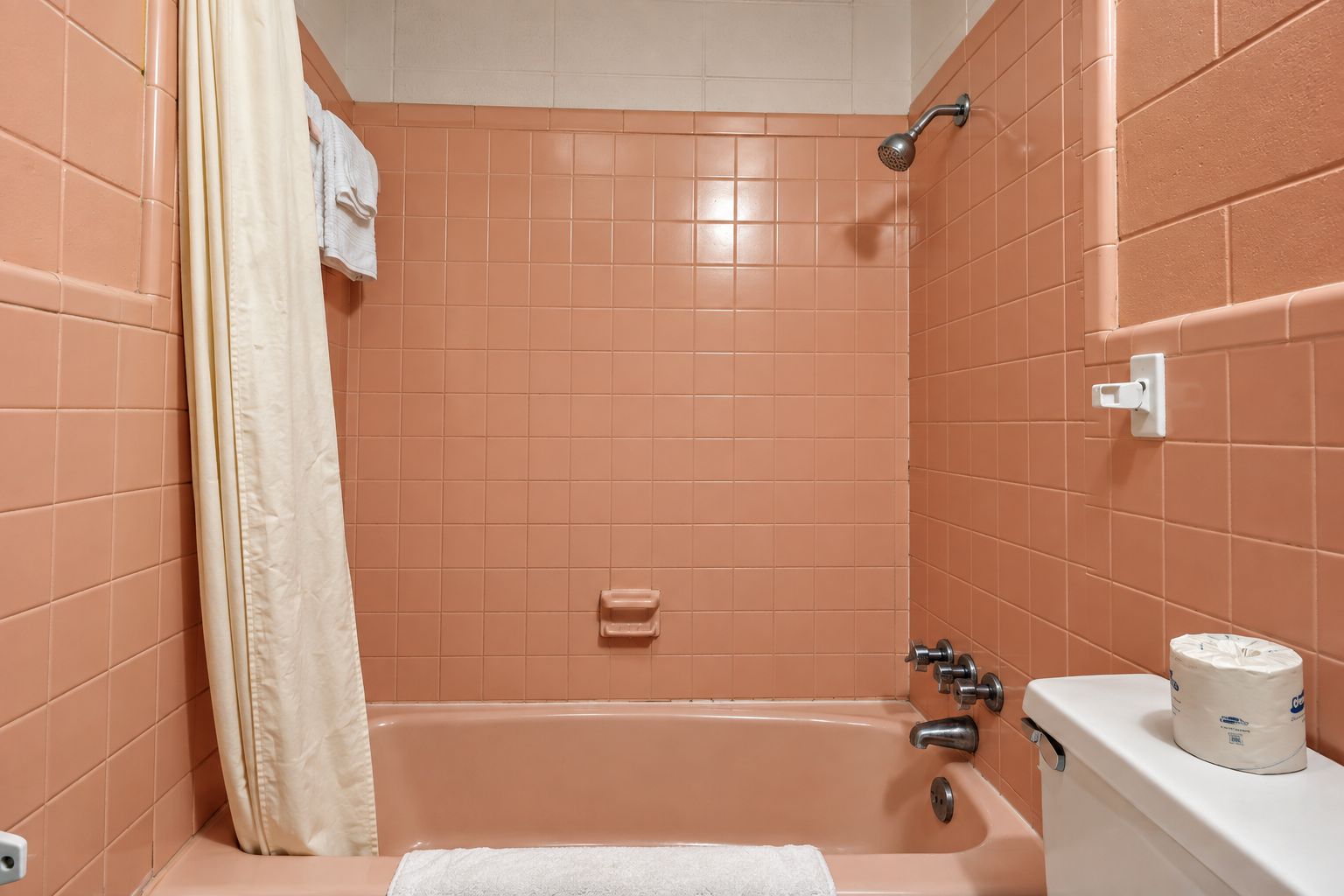 A bathroom with a bathtub, a showerhead, a toilet, and a towel rack.