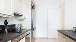 Une cuisine moderne avec des meubles blancs, un réfrigérateur en acier inoxydable et un plan de travail noir.