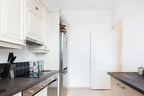 A modern kitchen with white cabinetry, a stainless steel refrigerator, and a black countertop. - Modern Apartment Close to Beach & City Centre (Cannes)