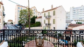Un balcon avec une table et une bougie, donnant sur une rue bordée d’immeubles et de voitures garées.