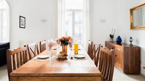 Une salle à manger avec une table en bois, des chaises, un vase rempli de fleurs et un panier de fruits.