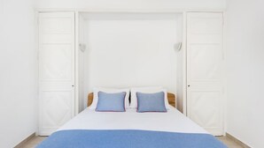 Une chambre à coucher avec un lit, deux oreillers, une couverture bleue et des murs blancs.