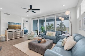 A modern living room with a television, sofa, ottoman, and a ceiling fan. - Coastal Charm by Coastal Chic Vacations (Bradenon)