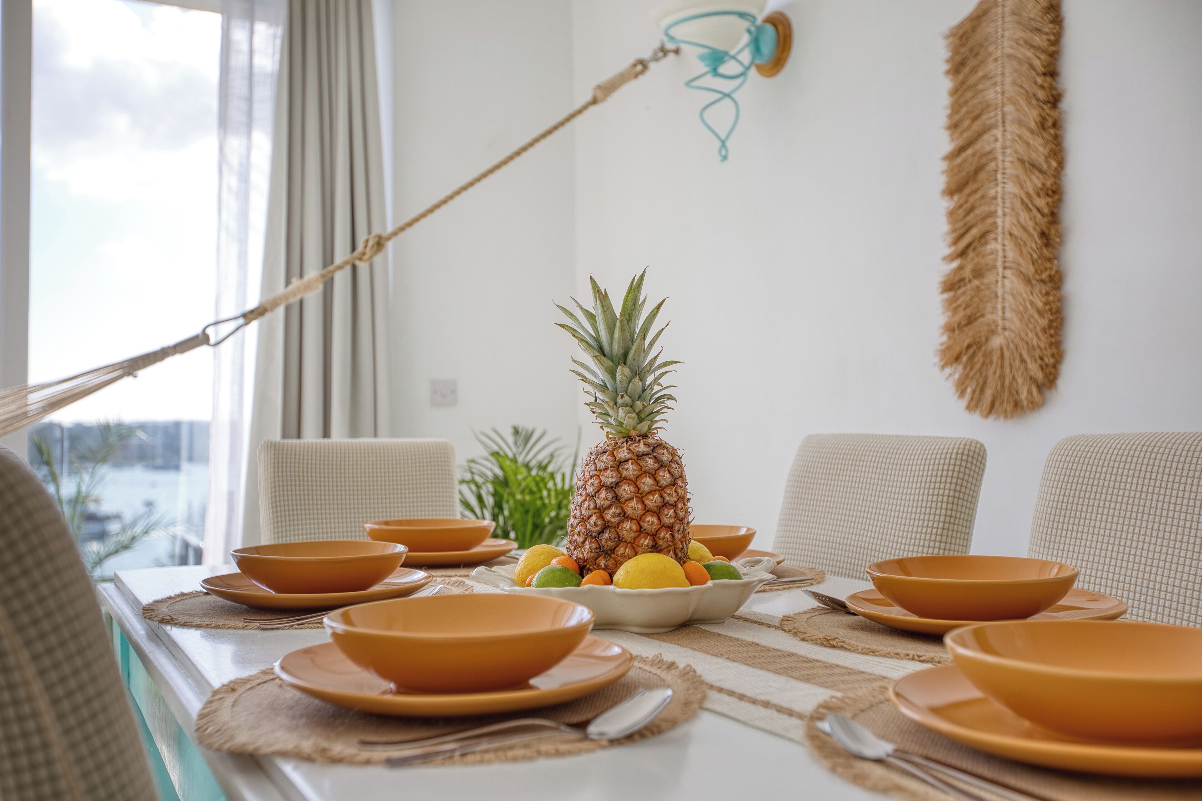A dining table set with orange bowls, a pineapple, and a bowl of fruit.
