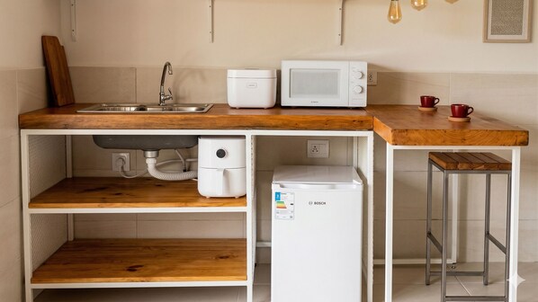 A compact kitchen with a sink, a microwave, a small refrigerator, and a wooden countertop.