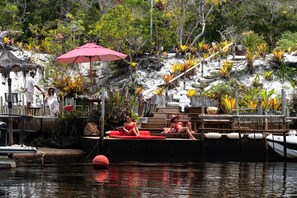 A water body with a dock, a red umbrella, and people relaxing. - CRISTAL DA MATA (Caraíva)