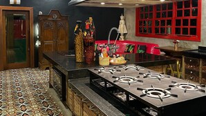 A kitchen with a patterned floor, a gas stove, wooden cabinets, and a red-framed window. - CRISTAL DA MATA (Caraíva)