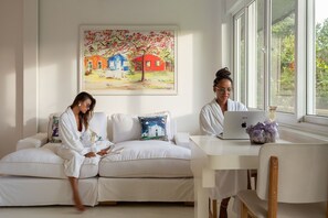 A room with a white sofa, a painting of houses, and a laptop on a table. - CRISTAL DA MATA (Caraíva)