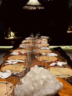 A long dining table set with multiple place settings, glasses, and a centerpiece of ice. - CRISTAL DA MATA (Caraíva)
