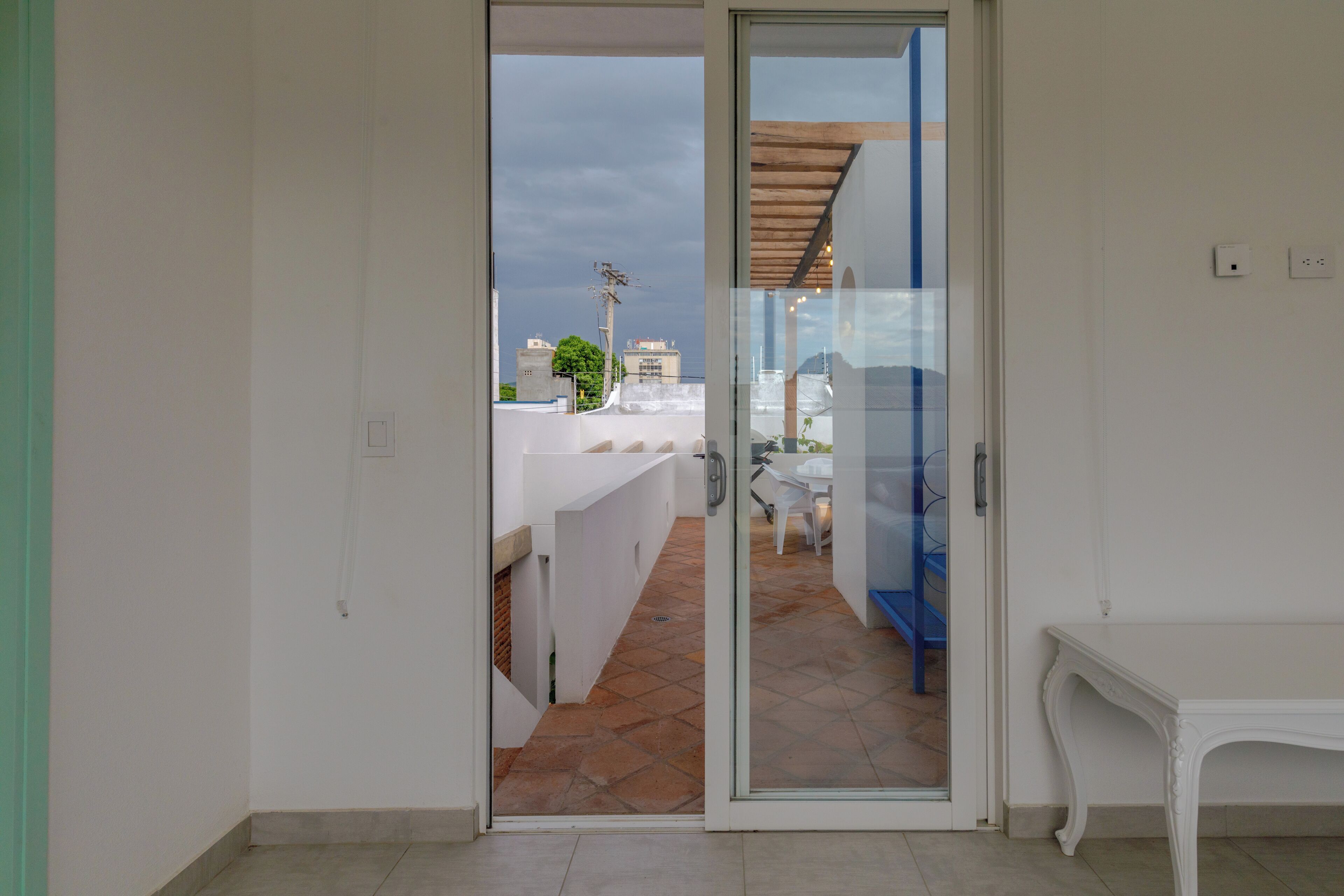 Habitación con puerta de vidrio corredera que da a un área exterior con patio, una mesa blanca y una silla azul.