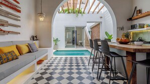Een moderne keuken met een geruit vloertje, een eethoek met barstoelen, een ingebouwde bank en uitzicht op een zwembad via een boog.