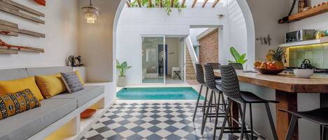 A modern kitchen with a checkered floor, a dining area with bar stools, a built-in bench, and a view of a pool through an archway.