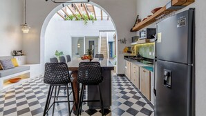 Een moderne keuken met een geruit vloertje, een centraal kookeiland, barkrukken, een koelkast en een hanglamp.