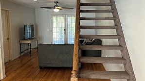 A staircase with wooden steps and a handrail, a ceiling fan, and a grey sofa in a room with wooden flooring.