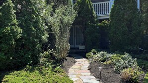 A stone pathway leading to a house surrounded by dense greenery.