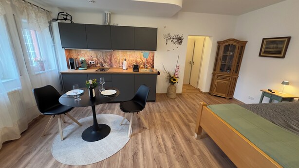 A compact room with a dining table, chairs, a bed, a kitchenette, and a cabinet. - MainNest Marktbreit - Cozy Apartment (Marktbreit)