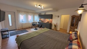 A compact hotel room with a bed, a small kitchenette, a dining area, and a separate entrance door. - MainNest Marktbreit - Cozy Apartment (Marktbreit)