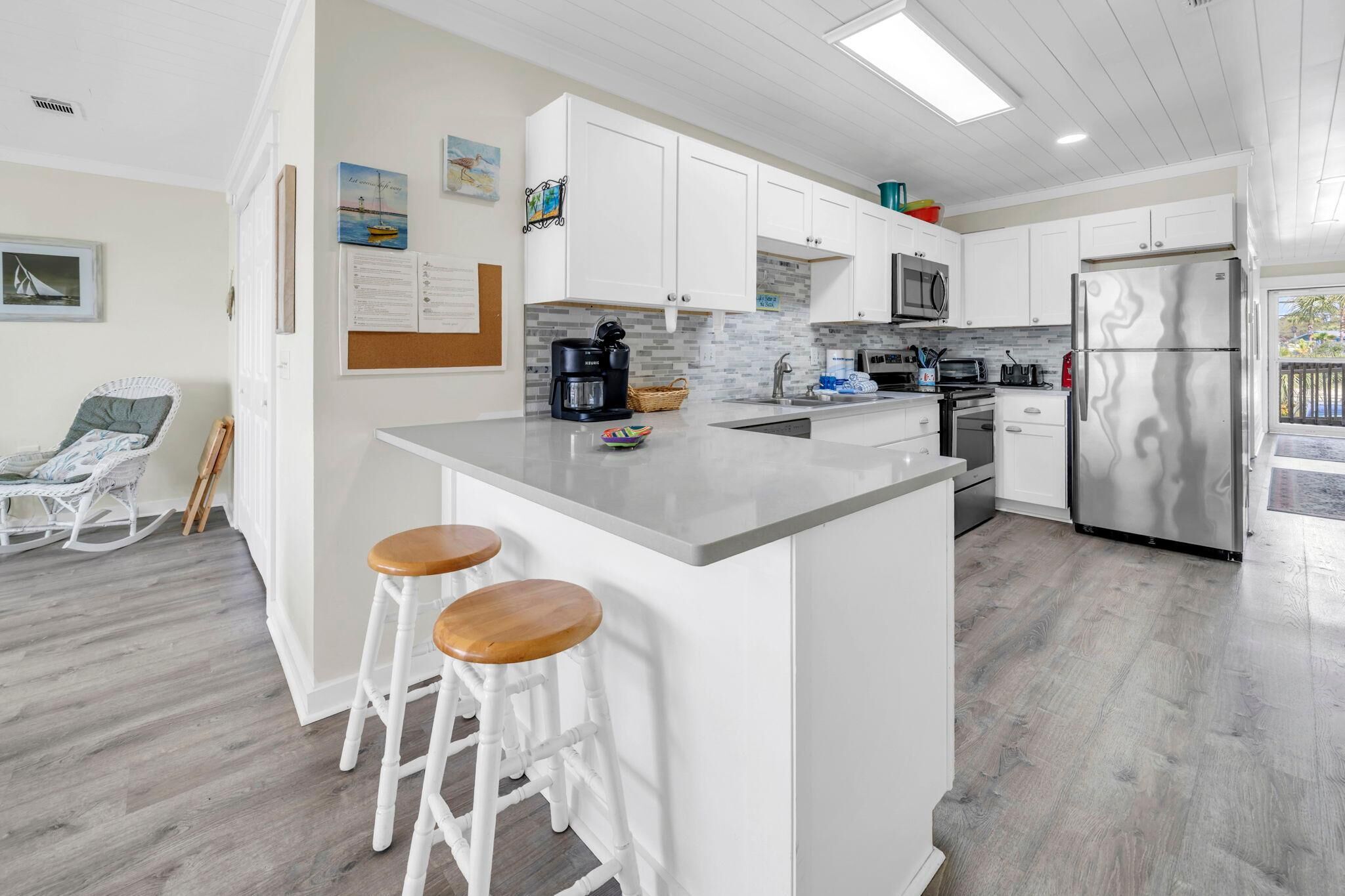 A modern kitchen with white cabinetry, a central island with stools, a stainless steel refrigerator, and a view to the outside.