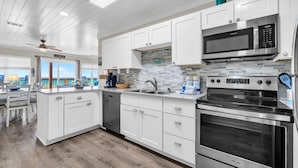 A modern kitchen with white cabinetry, a stainless steel microwave, and an oven. - Sands of Laguna B-1 (Panama City Beach)