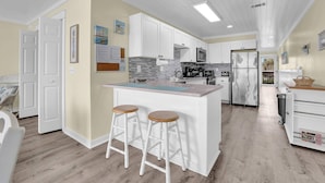 A kitchen with white cabinets, a stainless steel refrigerator, and a bar stool. - Sands of Laguna B-1 (Panama City Beach)