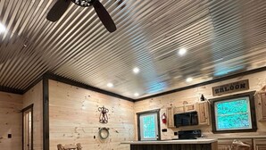 Un intérieur en bois avec un ventilateur de plafond, une table sur laquelle est posé un jeu de société et un téléviseur.