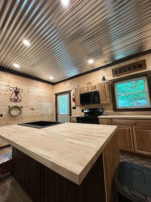 A kitchen with a wooden ceiling, a large island, and a window with a view of greenery.