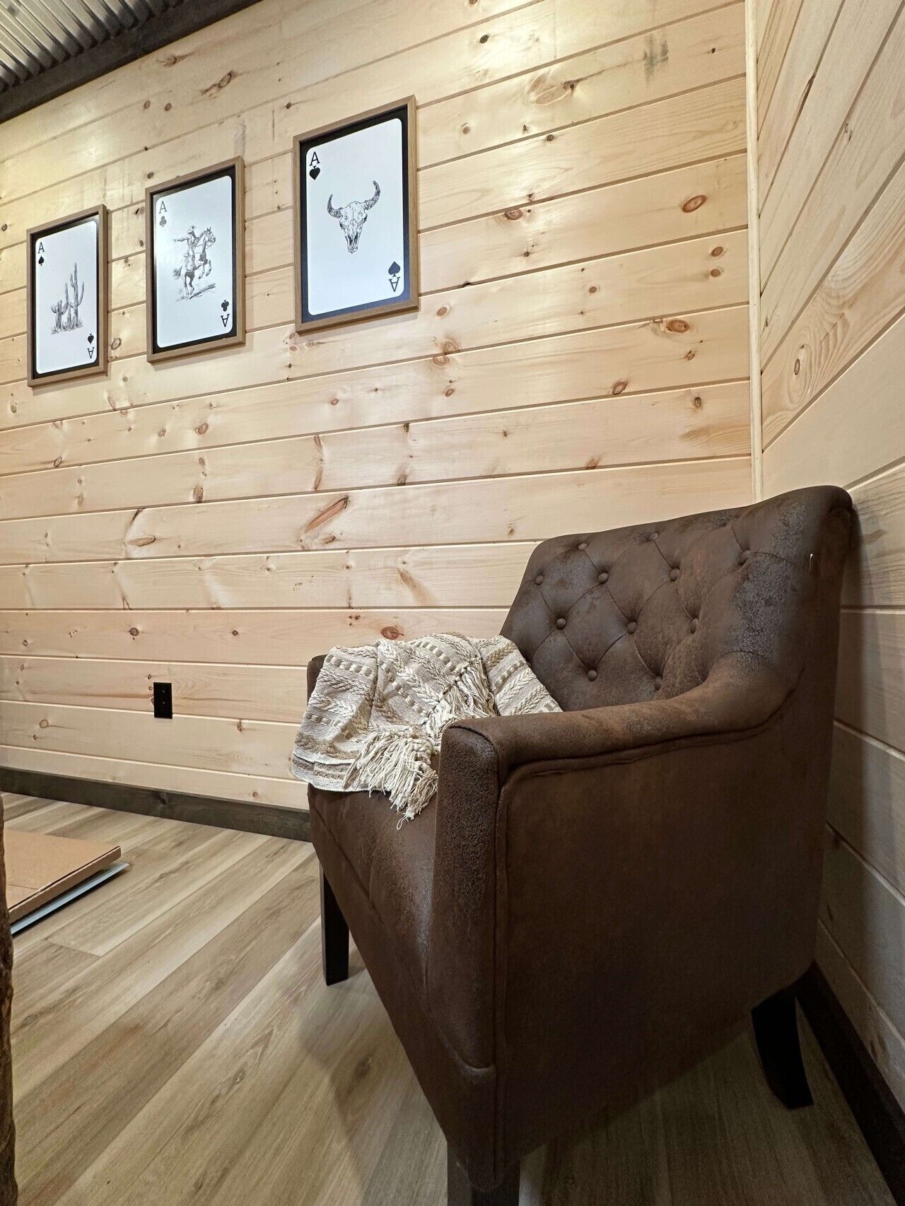 Een kamer met houten lambrisering, een bruine fauteuil en drie ingelijste kaartjes aan de wand.