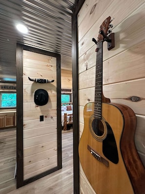 A wooden interior with a guitar, a bed, and a wall-mounted hat.