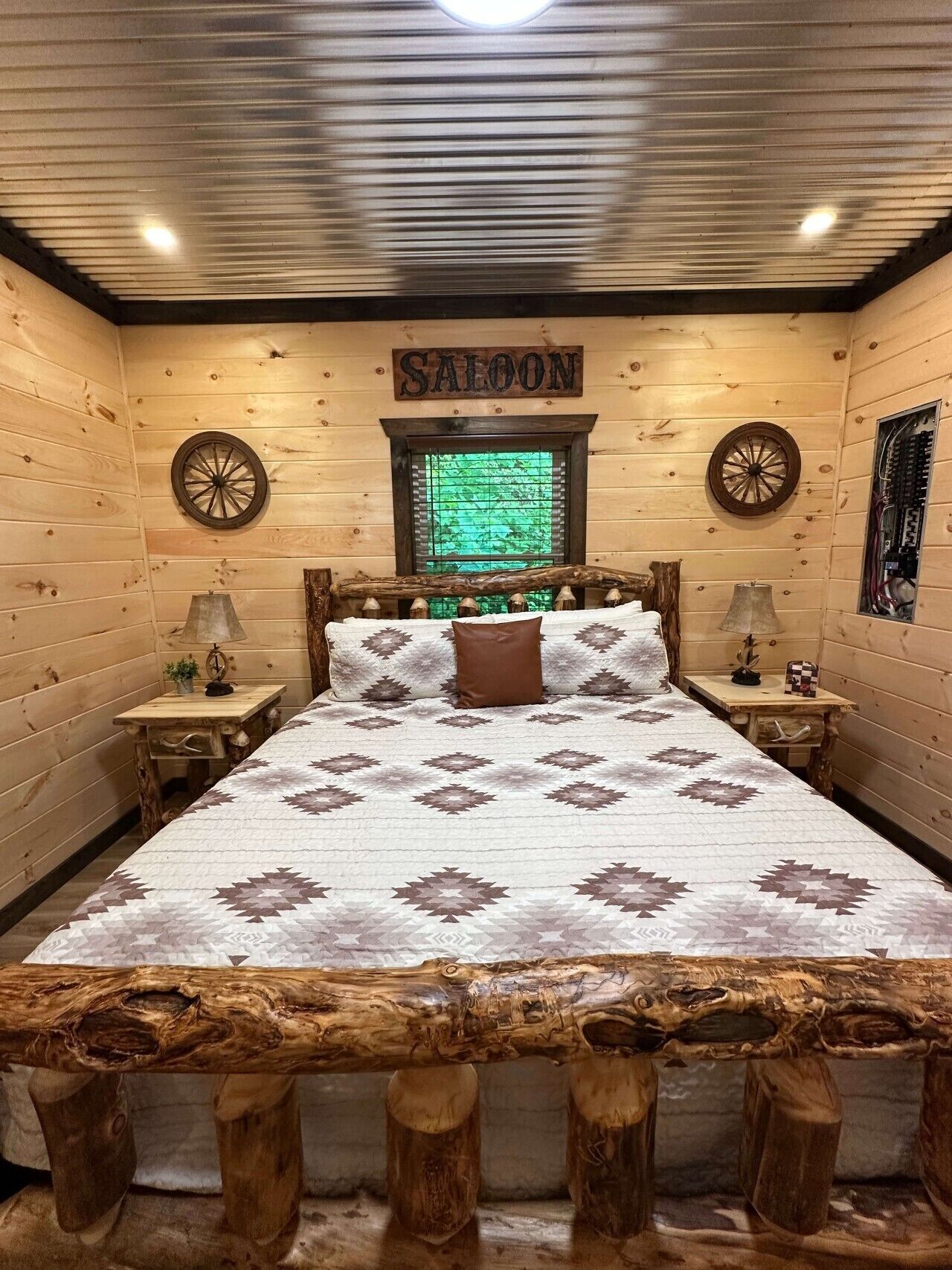 A log cabin-style room with a bed, two nightstands, a window with blinds, and a sign reading 'SALOON'.