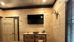 L’intérieur d’un chalet en bois comprend un lit, un téléviseur fixé au mur, une armoire en bois et une décoration représentant une tête de cerf.