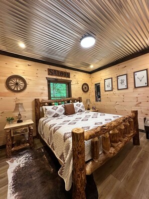 A rustic bedroom with a wooden bed, a nightstand, a lamp, a wall clock, and a sign that reads 'SALOON'.