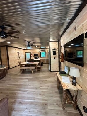 A rustic cabin interior with a dining area, kitchen, and a ceiling fan.