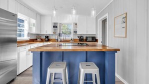 A modern kitchen with white cabinets, a wooden countertop, stainless steel appliances, and a blue accent wall. - The Blue Marlin (Panama City Beach)