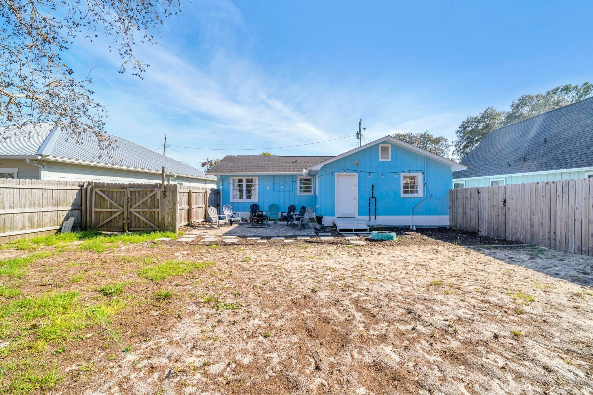 A blue house with a fenced backyard, a wooden gate, and outdoor seating.