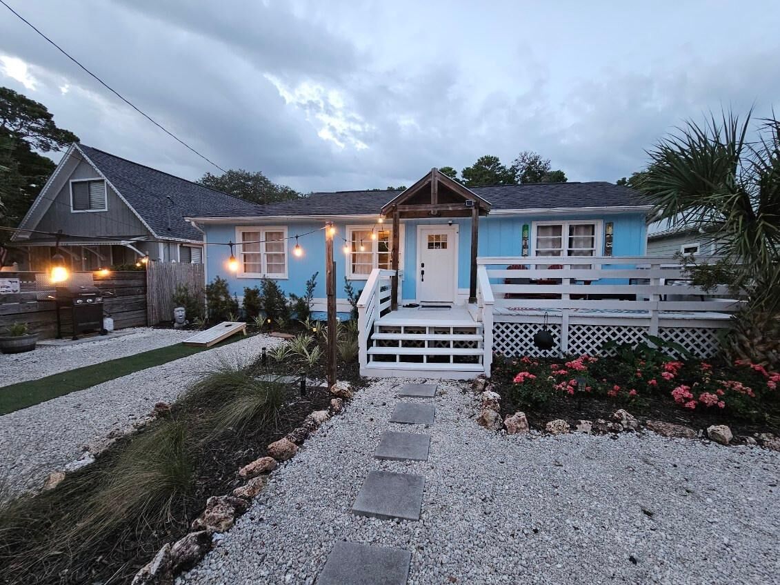 A two-story house with a front porch, a small deck, and a gravel pathway leading to the entrance.