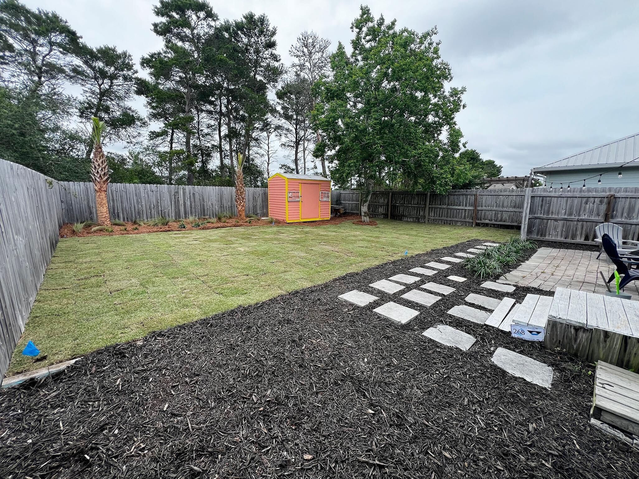 A backyard with a wooden fence, a small shed, and a paved walkway.