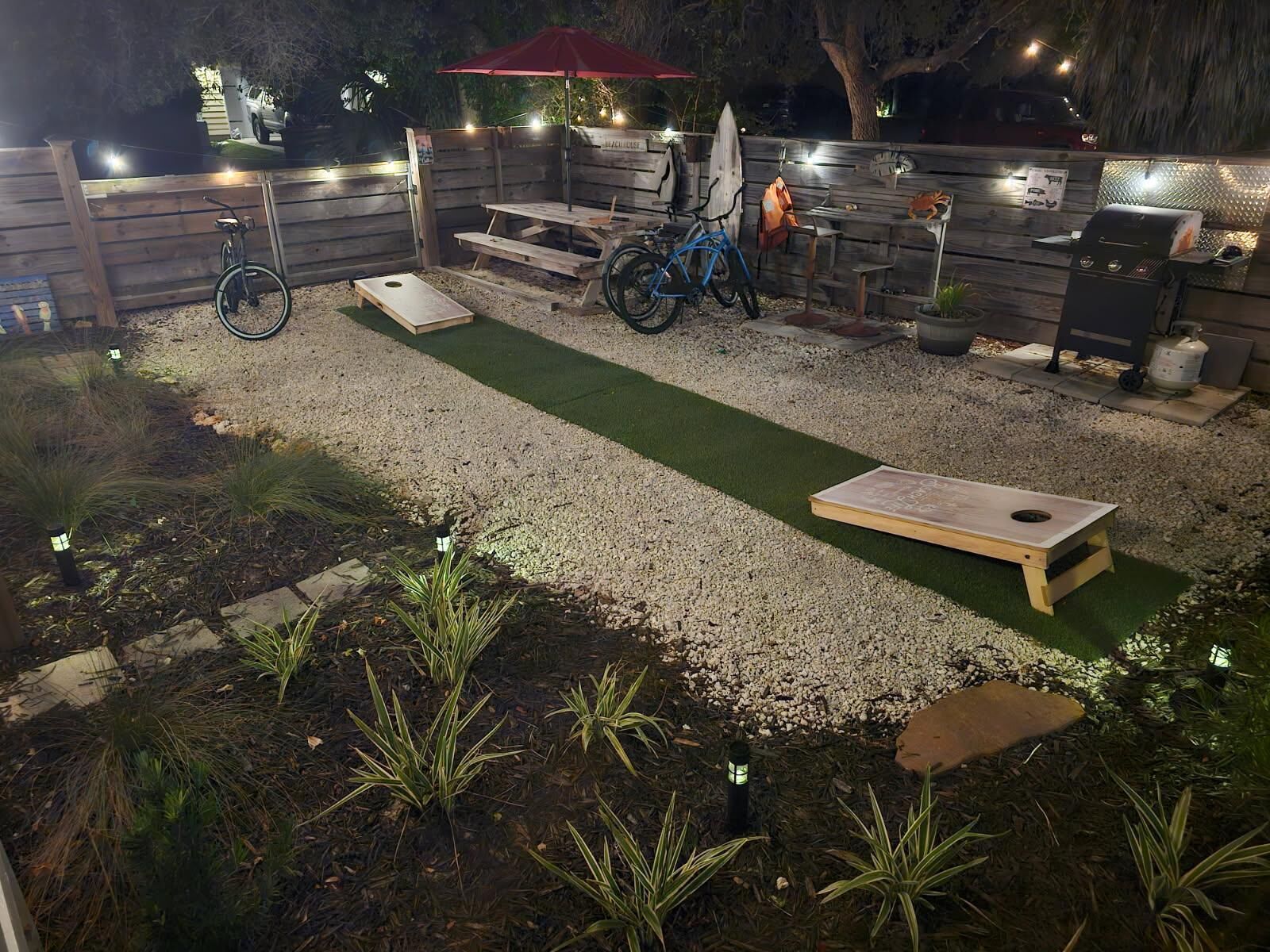 Un patio trasero con una terraza de madera, una parrilla, una bicicleta y un paraguas rojo.