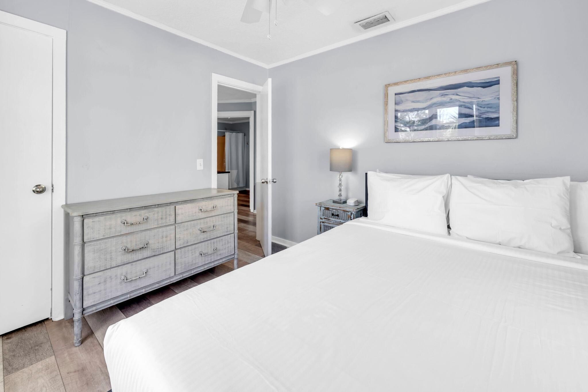 Une chambre à coucher avec un grand lit, une commode, une table de chevet et un tableau encadré au mur.