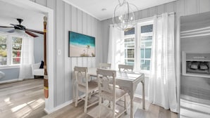 A dining area with a wooden table and chairs, a ceiling fan, a painting, and a refrigerator. - The Blue Marlin (Panama City Beach)