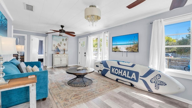 A living room with a blue sofa, a table, a surfboard, and a view of the ocean. - The Blue Marlin (Panama City Beach)