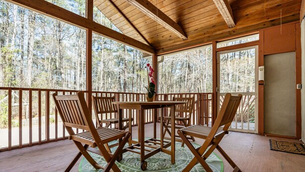 Een houten terras met tafel en stoelen, omgeven door een hekwerk, met uitzicht op een bebost gebied.