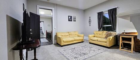 A living room with two yellow sofas, a patterned rug, a wooden side table, and a television on a stand.