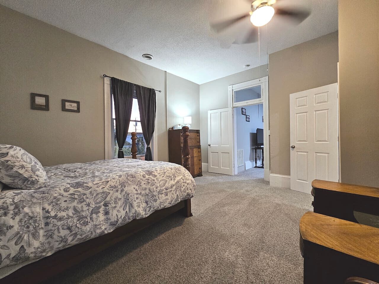 A bedroom with a bed, a ceiling fan, a dresser, and a door leading to another room.
