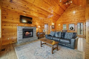 Ein Blockhaus-Interieur mit Kamin aus Stein, einer Ledersofa und einem an der Wand befestigten Fernseher.