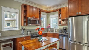A kitchen with wooden cabinets, a stainless steel refrigerator, a microwave, and a dining table with a vase of flowers. - Cozy Condo with a river views (Carrabelle)