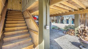 A wooden staircase leading to an upper level, a covered outdoor area with a gravel path, and a stack of firewood. - Cozy Condo with a river views (Carrabelle)