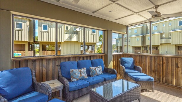 An outdoor patio with wicker furniture, a glass-top table, and a view of a row of cabins. - Cozy Condo with a river views (Carrabelle)